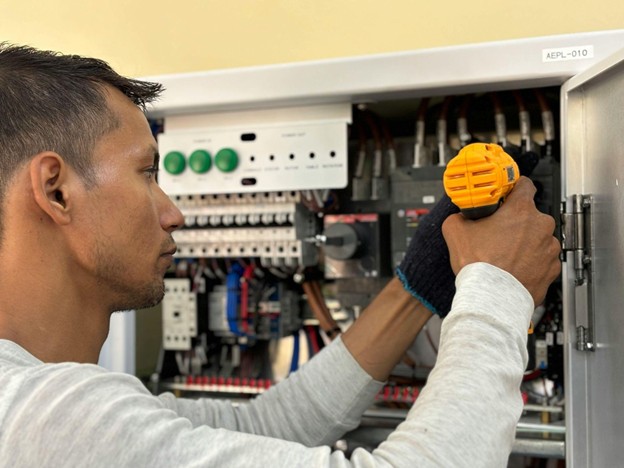 Electrician using a power tool to fix wiring inside a control box.