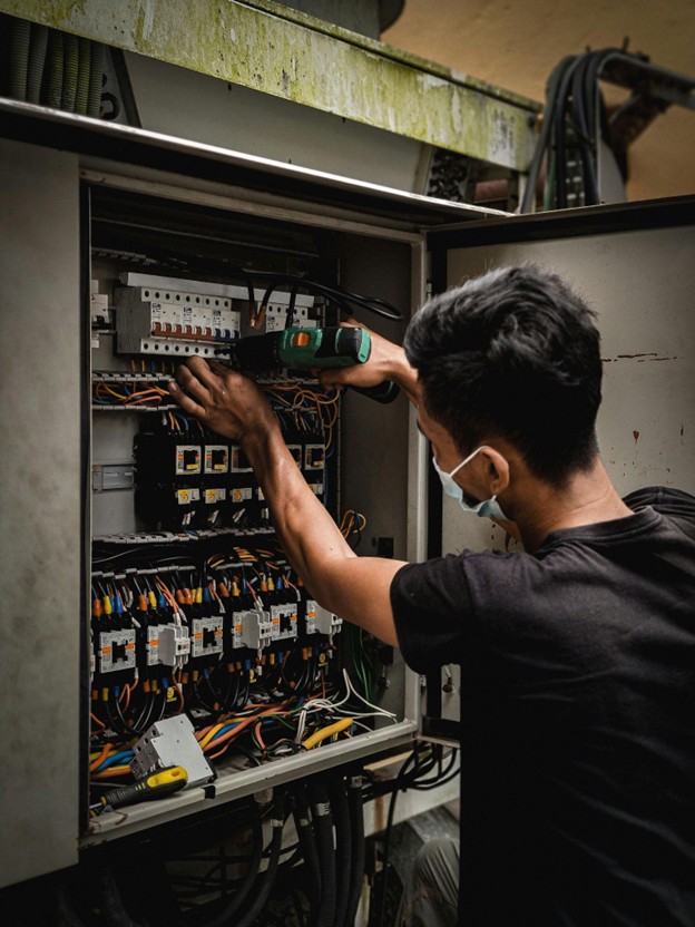 Man using a screwdriver to repair electrical panel wiring